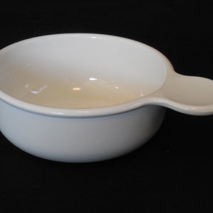 May include: A white ceramic bowl with a single handle. The bowl is round and has a smooth, glossy finish.