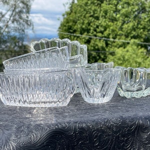 May include: A set of six clear glass bowls with a decorative, textured design. The bowls are arranged in a row on a black surface.