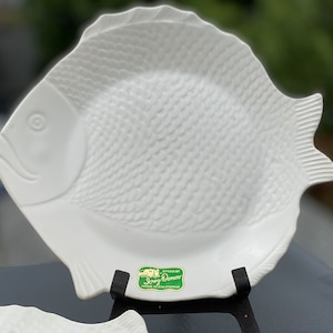 May include: White ceramic fish-shaped serving plate with a textured surface. The plate has a green label with the text "Syracuse China Made in California".