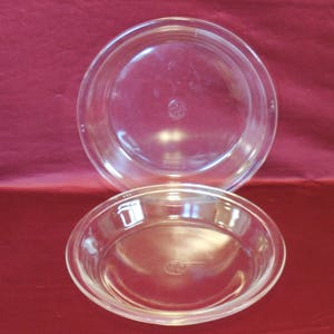May include: Two clear glass pie plates, one stacked on top of the other. The plates are round and have a fluted edge.