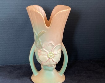 May include: A vintage, light pink and green ceramic vase with a floral design. The vase has two handles and a wide base.