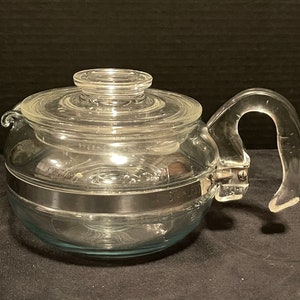 May include: A clear glass teapot with a stainless steel band around the middle and a clear plastic handle. The teapot has a blue tint to the glass.