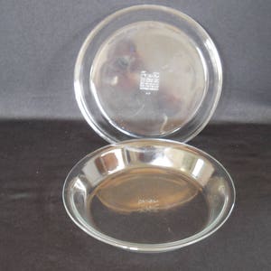 May include: Two clear glass pie plates, one stacked on top of the other. The bottom plate has the words "Pyrex Made in USA" printed on the bottom.