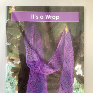 Peut inclure: Un livre intitulé "It's a Wrap" avec une écharpe en dentelle violette drapé sur un tronc d'arbre. La couverture du livre indique également "A Lace Guild Publication".