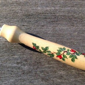 May include: A wooden tool with a silver metal tip and a painted design of green leaves and red berries.