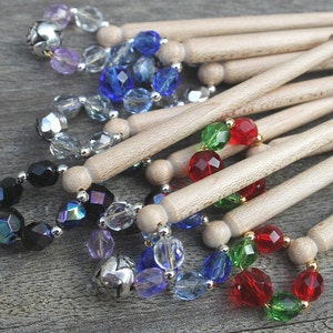 May include: A set of wooden knitting needles with colourful glass beads. The beads are in various colours, including red, green, blue, and black.