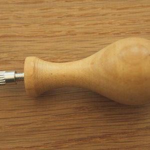 May include: A wooden handle with a metal knob on one end. The handle is light brown and has a smooth, rounded shape.