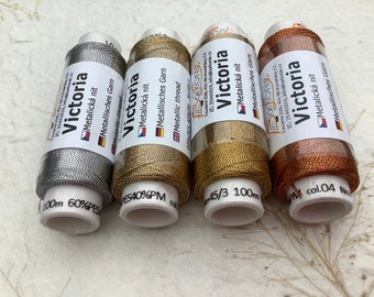 May include: Four spools of metallic thread in silver, gold, copper, and bronze. Each spool is labeled "Victoria" and has the text "Metalická nit" and "Metallisches Garn" printed on it. The spools are 100 meters long.