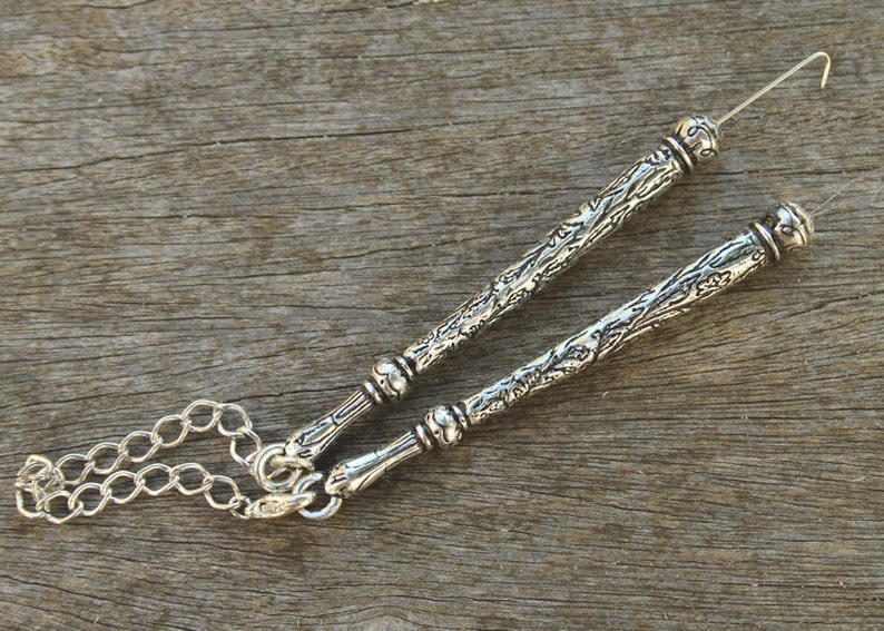 May include: A silver chain with two decorative silver rods attached. The rods have an ornate design and are connected to the chain with a loop at one end. The other end of each rod has a small loop.