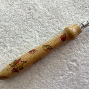 May include: A wooden pen with a silver top and a design of fall leaves in shades of red, orange, and yellow.