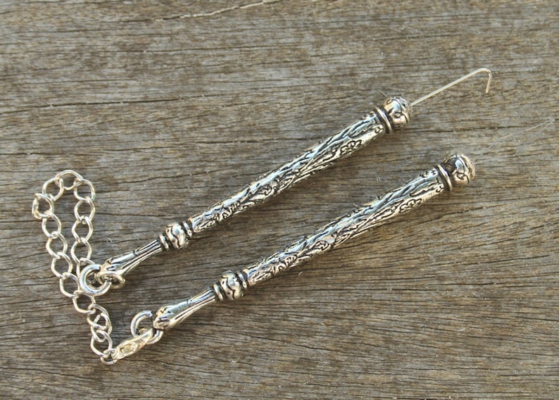 May include: Two silver ornate decorative sticks with a chain connecting them. The sticks have a floral design and are about 6 inches long.