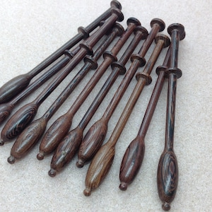 May include: A set of 12 wooden bobbins for lace making. The bobbins are brown with dark brown stripes and have a smooth, polished finish.