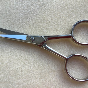 May include: A pair of small, silver-toned scissors with rounded handles. The blades are sharp and pointed.