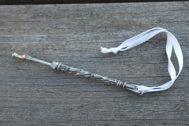 May include: A silver thimble with a decorative design and a white ribbon attached to it.