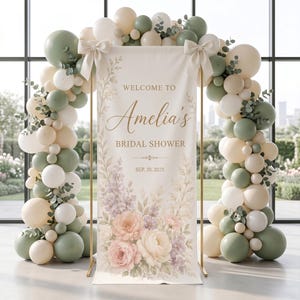 以下が含まれることがあります： 「WELCOME TO Amelia's BRIDAL SHOWER SEP. 20, 2025」という文字と花のイラストが描かれたブライダルシャワー用の縦型バナー。セージグリーン、クリーム、ホワイトのバルーンアーチで囲まれ、2つの大きなリボンが飾られています。