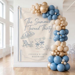 Puede incluir: Un telón de fondo rectangular de cumpleaños con una escena de playa, una sombrilla a rayas, una tumbona y copas de cóctel. El texto dice The Summer I Turned Thirty y JESSICA'S 30TH BIRTHDAY. Un arco de globos en azul, beige y dorado enmarca el lado derecho.