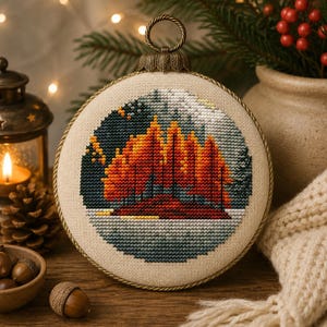 May include: A circular cross-stitch ornament featuring a landscape of vibrant orange and red autumn trees against a dark blue sky and a snowy ground. The embroidery is set in a round frame with a metallic bronze hanging loop and rope trim.