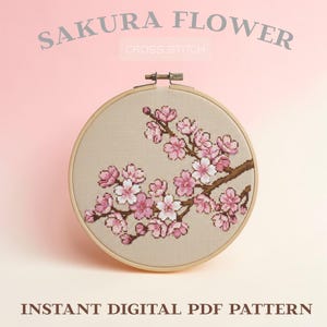 Puede incluir: Un bastidor de bordado de punto de cruz con un diseño de flor de cerezo. El diseño incluye flores rosas y blancas sobre ramas marrones, sobre un fondo beige. El texto "SAKURA FLOWER" y "CROSS STITCH" están en la parte superior, con "INSTANT DIGITAL PDF PATTERN" en la parte inferior.