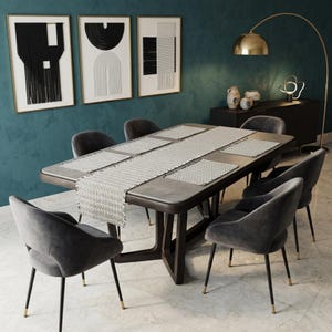 May include: A contemporary dining set featuring a dark wood table, six grey velvet chairs, and a patterned table runner. Three framed abstract artworks adorn the teal wall. A gold floor lamp and a black sideboard complete the room's decor.