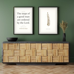 May include: Two framed wall art prints with white backgrounds. The left print features black text reading The steps of a good man are ordered by the Lord. Psalm 37:23 ordered steps. The right print displays a brown botanical leaf illustration.