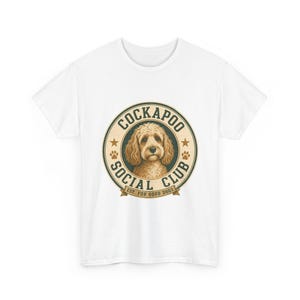 May include: A white short-sleeve t-shirt featuring a circular graphic on the chest. The design includes a tan Cockapoo dog illustration surrounded by the text COCKAPOO SOCIAL CLUB and the phrase EST. FOR GOOD DOGS with small paw prints.
