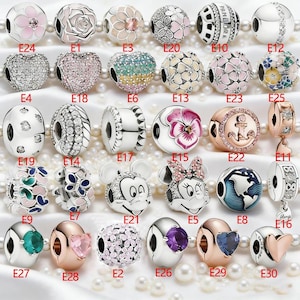Puede incluir: Una colección de treinta cuentas tipo charm de plata y oro rosa dispuestas en cinco filas, cada una etiquetada con un código alfanumérico de E1 a E30, con diversos diseños que incluyen motivos florales, corazones, gemas y personajes.