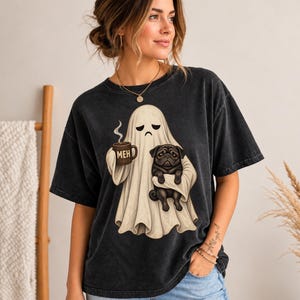 May include: A charcoal black, acid-wash t-shirt featuring a graphic of a beige ghost with a sad expression. The ghost holds a brown mug with the text MEH printed on it and carries a small black pug dog in its arms against a dark background.