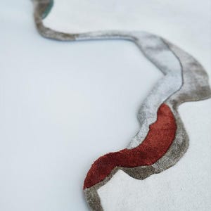 Könnte beinhalten: Weißer Teppich mit einem abstrakten Design in einer fließenden, organischen Form. Das Design integriert Grautöne, einen Hauch von Türkis und einen kräftigen roten Akzent, wodurch eine moderne und künstlerische Ästhetik entsteht.