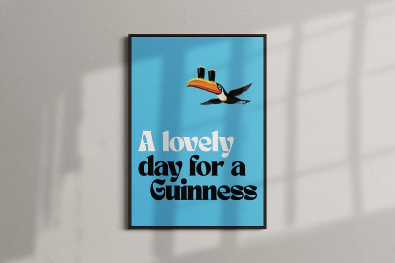 May include: A framed poster with a light blue background features a toucan carrying two pints of Guinness. The text "A lovely day for a Guinness" is displayed in white and black fonts.