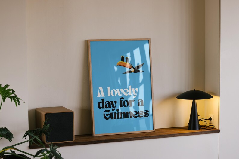 May include: A framed poster with a light blue background and the text "A lovely day for a Guinness." A toucan illustration is above the text. A black lamp and a wooden speaker are on a shelf.