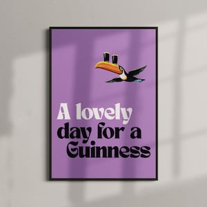 K&ouml;nnte beinhalten: Gerahmtes Poster mit lila Hintergrund. Es zeigt einen Tukan mit zwei Guinness-Pints und dem Text "A lovely day for a Guinness" in Wei&szlig; und Schwarz.
