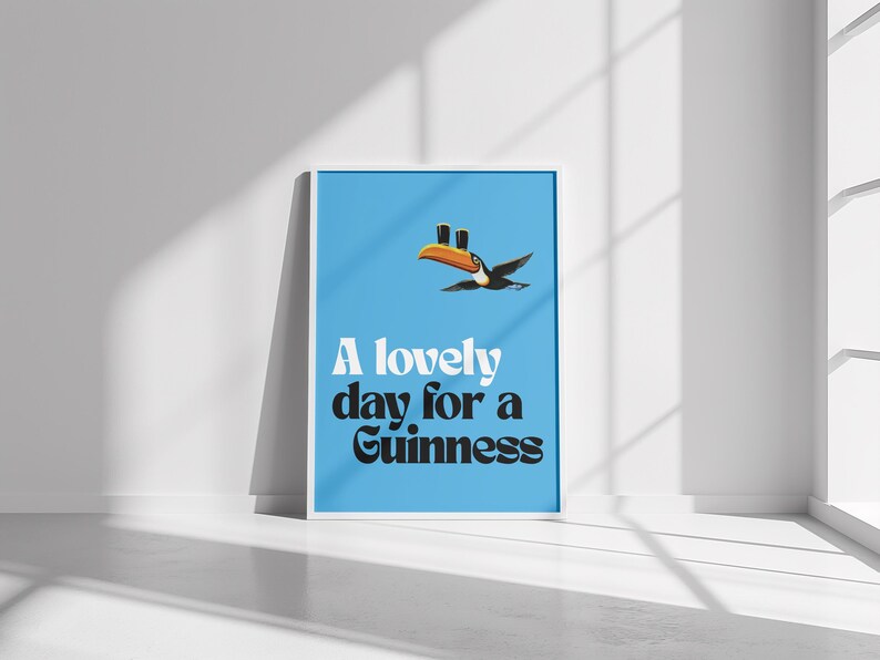 May include: Framed poster with a light blue background featuring a toucan carrying two pints of Guinness. The text "A lovely day for a Guinness" is displayed in white and black font.