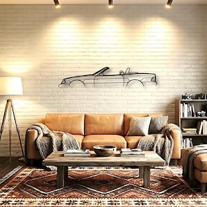 May include: A black metal wall art piece featuring the minimalist outline of a convertible car. The linear design depicts the side profile of the vehicle, including the windshield, open top, and wheel arches, mounted on a white brick wall.