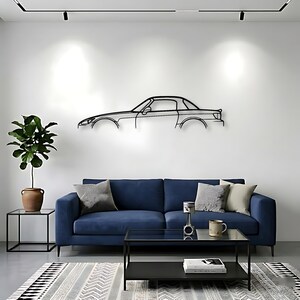 May include: A black metal car outline wall art decor above a blue sofa. The car art is mounted on a white wall. A black coffee table, a potted plant, and a patterned rug complete the living room setting.