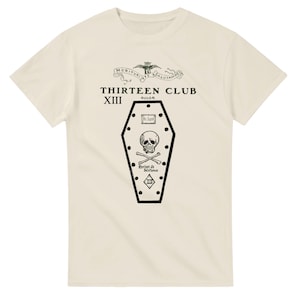 May include: Cream-coloured t-shirt with a black coffin graphic, skull and crossbones, and the text "THIRTEEN CLUB". Above the text is a banner with the words "MORITURI TE SALUTAMUS".