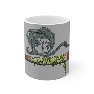 May include: A white ceramic mug with a gray background. The mug features a stylized design of a smoking object with the word "KNOWLEDGE" in yellow dripping letters. The design includes a gray smoke-like shape and red accents.