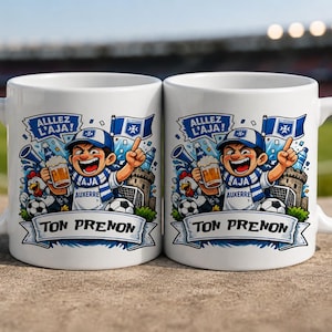 Peut inclure: Deux tasses en céramique blanche ornées d'une illustration de dessin animé colorée représentant un supporter de football avec une écharpe et une casquette bleu et blanc, tenant une chope de bière. Le texte "ALLEZ L'AJA!" et "TON PRENON" est présent.