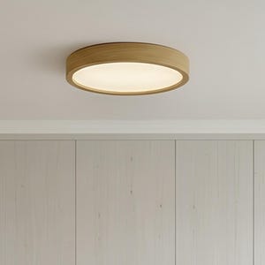 Può includere: Una cucina moderna con mobili in legno chiaro, un piano di lavoro bianco e tre sgabelli in legno con sedute intrecciate. Un apparecchio di illuminazione rotondo a incasso illumina lo spazio. La cucina è dotata di un piano cottura integrato e una macchina per il caffè.