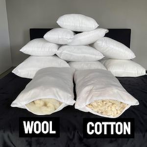 Könnte beinhalten: Eine Ansammlung weißer Kissen, einige gestapelt, andere geöffnet, um Woll- und Baumwollfüllung zu zeigen. Die Wörter "WOOL" und "COTTON" werden darunter angezeigt, um die verschiedenen Materialien hervorzuheben.