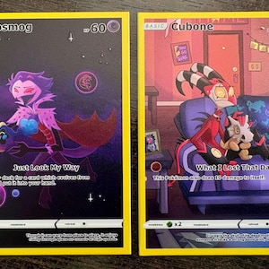 May include: Two rectangular trading cards with yellow borders. The left card features a purple character holding a small creature in space with the text Just Look My Way. The right card shows a red character on a couch with a skull-headed creature and the text What I Lost That Day.