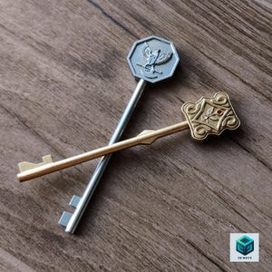 May include: Two decorative keys crossed over each other. One key is silver-toned with an octagonal head featuring an eagle emblem. The other key is gold-toned with an ornate, rectangular head featuring a small red accent and an eagle motif.