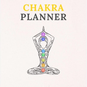May include: A white planner with the words "CHAKRA PLANNER" in yellow and gray. The cover features a black and white illustration of a person in a yoga pose, with colorful chakra symbols aligned along the body.