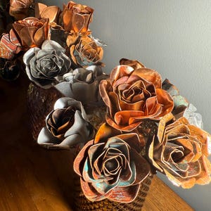 May include: A decorative arrangement of metal roses in shades of copper, bronze, and silver. The flowers are arranged in a textured, bronze-colored vase. The roses have intricate details and varying patinas, creating a unique and artistic display.