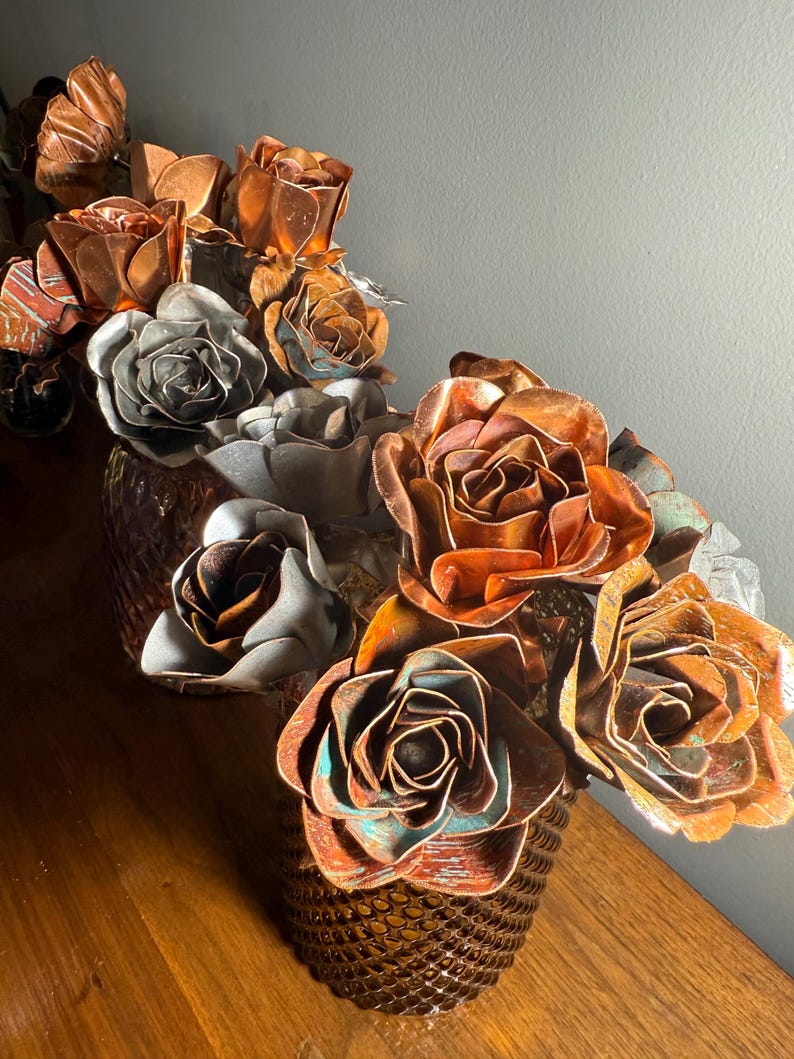 May include: A decorative arrangement of metal roses in shades of copper, bronze, and silver. The flowers are arranged in a textured, bronze-colored vase. The roses have intricate details and varying patinas, creating a unique and artistic display.