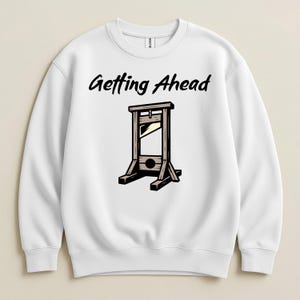 May include: White sweatshirt with the text "Getting Ahead" above a cartoon guillotine illustration. The guillotine is brown and black, with a blade and a wooden frame. The sweatshirt is a crew neck style.