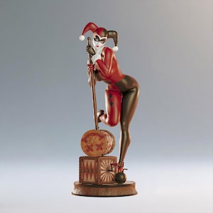 Könnte beinhalten: Figur einer Figur in einem rot-schwarzen Kostüm, die sich auf einen Holzhammer stützt. Die Figur hat eine weiße Maske und eine Narrenkappe. Der Sockel ist eine Holzkiste mit rundem Sockel und einer kleinen schwarzen Bombe.