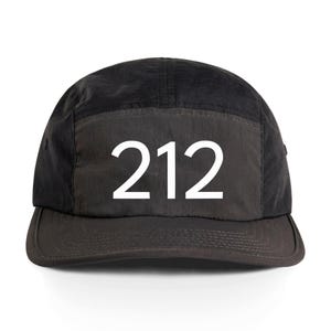 Może przedstawiać: Czarna czapka z pięcioma panelami i płaskim daszkiem. Na przodzie czapki widnieje biały numer "212". Kapelusz wykonany jest z ciemnego materiału, prawdopodobnie nylonu.