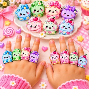 Può includere: Una collezione di otto anelli colorati con disegni di cupcake in stile cartoon con facce sorridenti, ciliegie e fiocchi. Ogni anello presenta una combinazione di colori pastello unica, tra cui blu, verde, rosa e viola, con motivi decorativi di cuori e stelle.