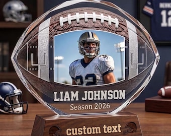 May include: A clear acrylic football-shaped trophy featuring a brown textured football graphic with white laces, a central photo of a football player, and the text LIAM JOHNSON Season 2026. The base is dark wood with the engraved text custom text.