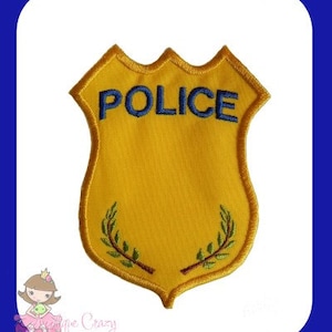 May include: A yellow felt police badge with a blue embroidered "POLICE" inscription and green embroidered laurel wreaths on the bottom.